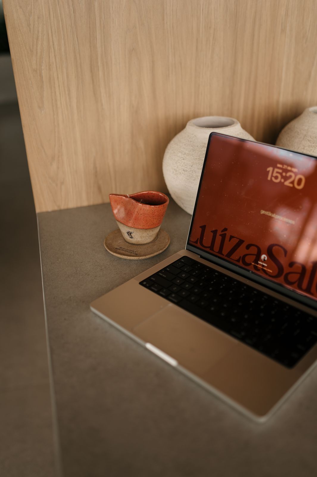 Notebook com a marca Luíza Sales na tela, ao lado da xícara da marca