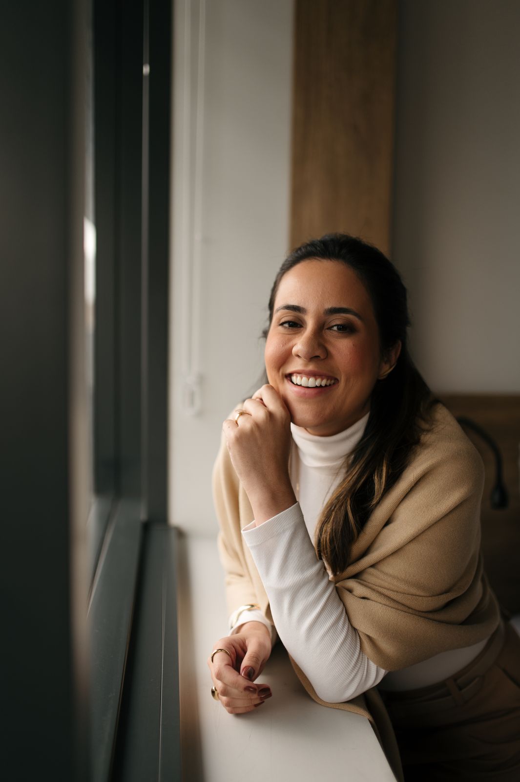 Luíza Sales sorrindo, apoiada na janela